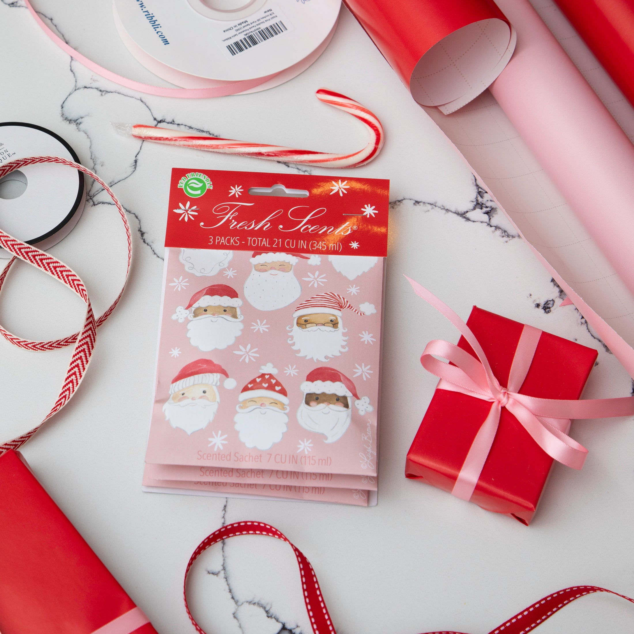 Pack of pink scented sachets with watercolor santas on it displayed on a marble background with gift wrapping supplies