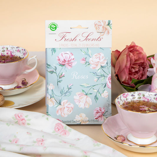 A pack of scented sachets with a floral design, labeled 'Roses', displayed on a table with a cup of tea and roses in the background.