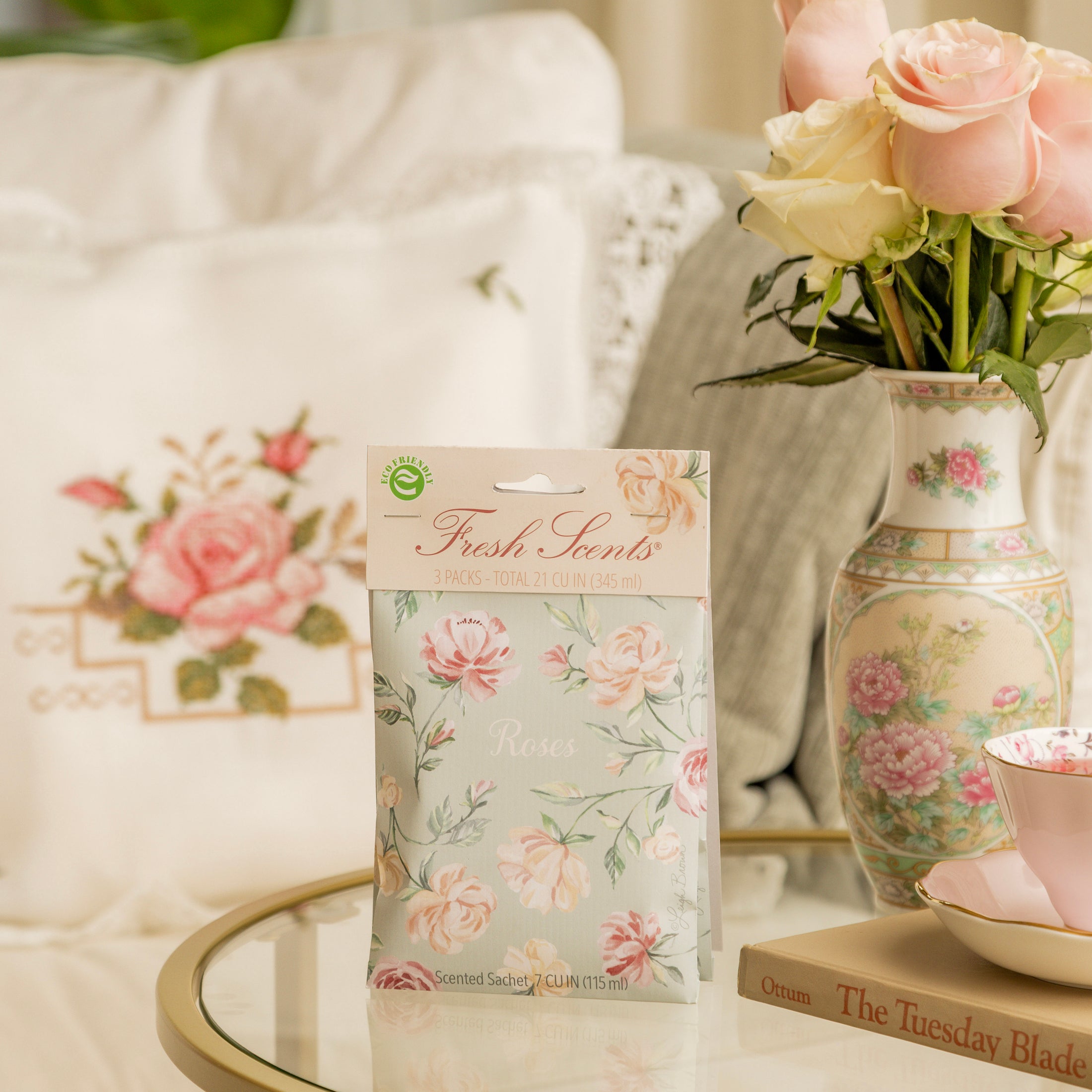 A pack of scented sachets with a floral design, labeled 'Roses', displayed on a glass table with a chinoiserie vase of roses.