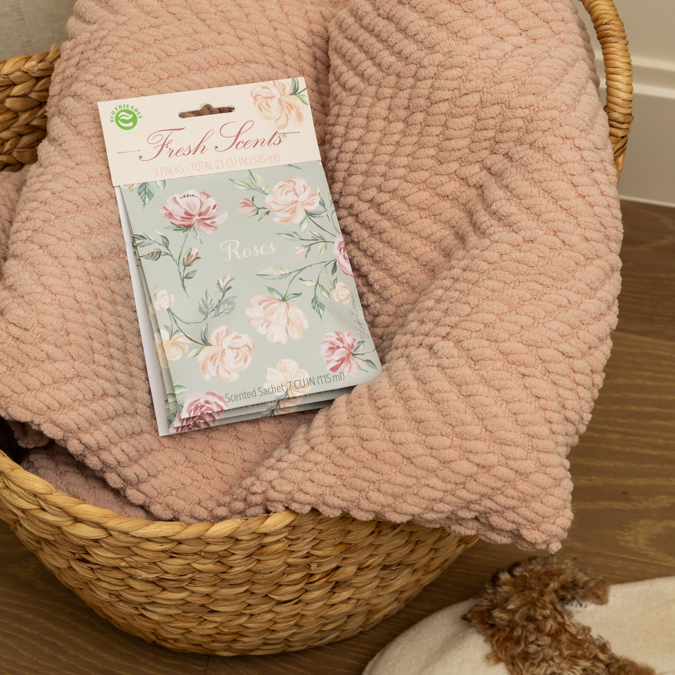 A pack of scented sachets with a floral design, labeled 'Roses', displayed in a woven basket with a mauve blanket