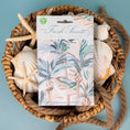 Load image into Gallery viewer, A scented sachet with a palm leaf watercolor design, placed on in a woven basket with seashells