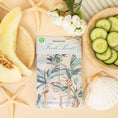 Load image into Gallery viewer, A scented sachet with a palm leaf design, placed on a surface with a starfish, slice of melon, and a bowl of cucumber slices.