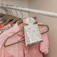 Load image into Gallery viewer, A closet rod holds several shirts on hangers, including a pink striped one. A Fresh Scents Roses - Sachet 3pk hangs among the clothes, adding a long-lasting, flameless rose fragrance to your wardrobe.