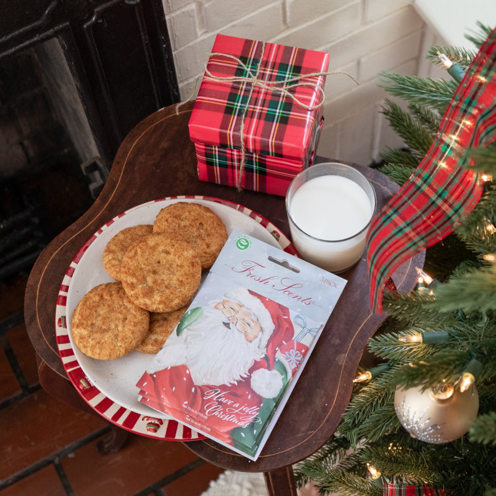 A pack of three scented sachets with a Christmas-themed design, featuring Santa Claus and displayed on a table with milk and cookies