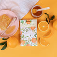 Load image into Gallery viewer, A scented sachet pack with water color oranges on it being displayed on an orange background with slices of orange and a jar of honey