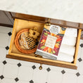 Load image into Gallery viewer, Open bathroom drawer with neatly folded white towels, a braided rope, and Fresh Scents' Love with Fall - Sachet 3pk—a decorative box of autumn leaf-scented sachets—plus a wooden massager, honey dipper, marble countertop, and tiled floor.