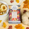 Load image into Gallery viewer, The Fresh Scents Love with Fall - Sachet 3pk, adorned with "Every year I fall in love with fall," sits on a yellow background among autumn leaves, a white pumpkin, and caramel pears—a charming flameless fragrance for your space.