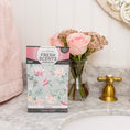 Load image into Gallery viewer, A box of Fresh Scents Roses - Sachet 3pk brings long-lasting, flameless fragrance to a marble bathroom counter, placed beside a vase of pink roses and a gold faucet, with a pink towel in the background.