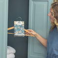 Load image into Gallery viewer, Someone places a Live in the Moment - Sachet 3pk by Fresh Scents on a wooden hanger inside a blue cabinet with folded white towels, bringing long-lasting freshness to the space.