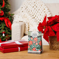 Load image into Gallery viewer, A package of Fresh Scents’ Peace on Earth - Sachet 3pk sits on a wooden table beside red poinsettias and wrapped gifts, with a Christmas tree and cream-colored knit blanket in the background. These sachets deliver long-lasting, flameless fragrance from Fresh Scents that elevates your holiday ambiance.
