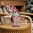 Load image into Gallery viewer, A glittery reindeer and Fresh Scents Red Door Wreath Sachet 3pk are displayed on a round wooden table with stacked books in a cozy, holiday-themed living room, featuring a plaid blanket and decorated Christmas tree.