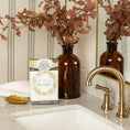 Load image into Gallery viewer, A marble bathroom counter with a brass faucet, brown glass vase with dried leaves, gold leaf-shaped dish, white towel, and Fresh Scents Lets Stay Home - Sachet 3pk for flameless fragrance and long-lasting air freshening.