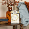 Load image into Gallery viewer, The Fresh Scents Lets Stay Home - Sachet 3pk rests on a table beside books, an amber vase with autumn leaves, and cozy décor, providing long-lasting, flameless fragrance for your space.