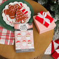 Load image into Gallery viewer, A plate of gingerbread cookies, a Fresh Scents Merry Santas Sachet 3pk in pink, and a pink gift box with a white ribbon sit on a round wooden table by the Christmas tree and red-and-white cloth.