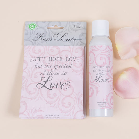 A product image featuring a 3-pack of sachets and a room spray bottle, both with the 'Faith Hope Love' fragrance. The sachets are pink with floral patterns and the spray bottle is white with a pink label.