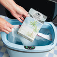 Load image into Gallery viewer, A person holds a Fresh Scents Seaspray - Sachet 3pk, a flameless fragrance, over an open blue trash can lined with a white bag, ready to dispose of the sachet.
