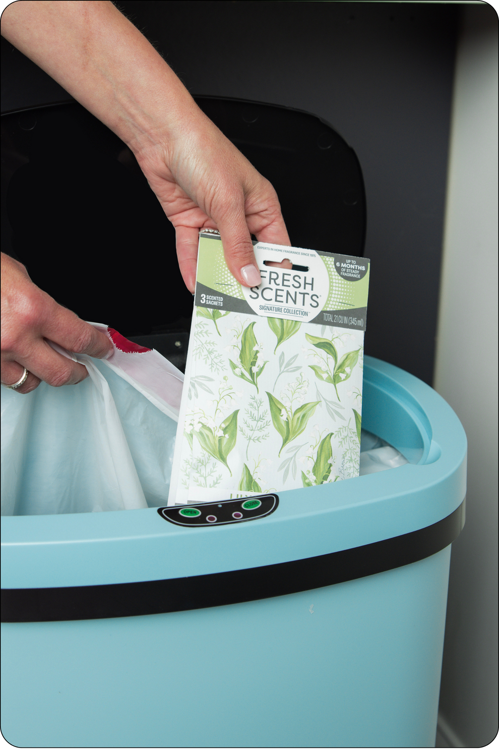 Person placing a 'Fresh Scents' Lily of the Valley sachet into a trash bin.