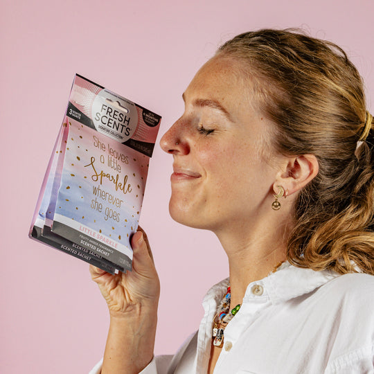 Woman holding a 'Fresh Scents' scented sachet on a pink background