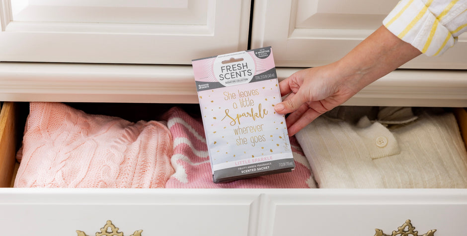Hand placing a 'Fresh Scents' sachet into a drawer with pink fabric and white cabinet.