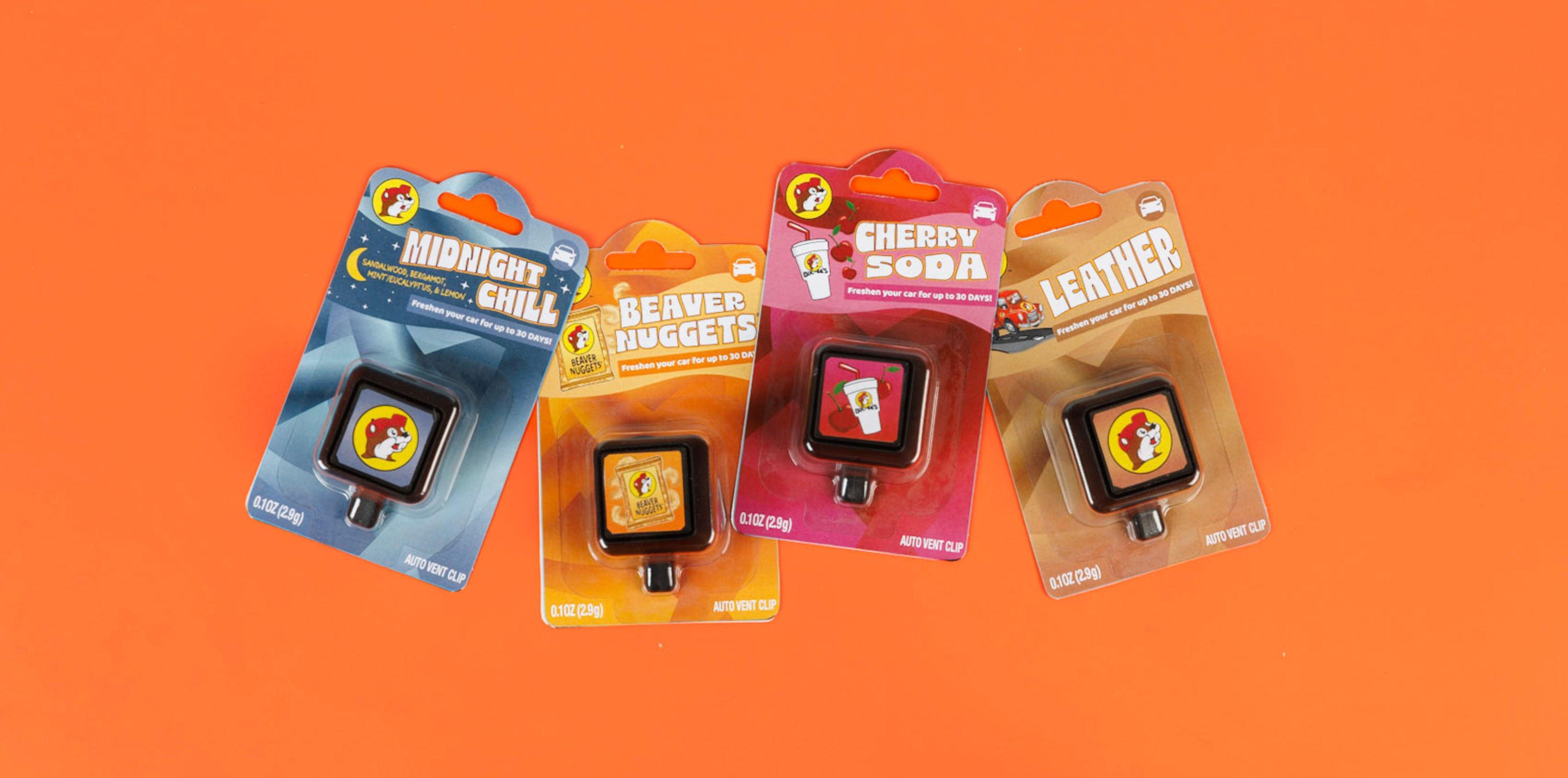 Four packaged scented air fresheners are displayed against an orange background. The scents are Midnight Chill, Beaver Nuggets, Cherry Soda, and Leather, each with colorful graphics and a beaver mascot on the packaging.