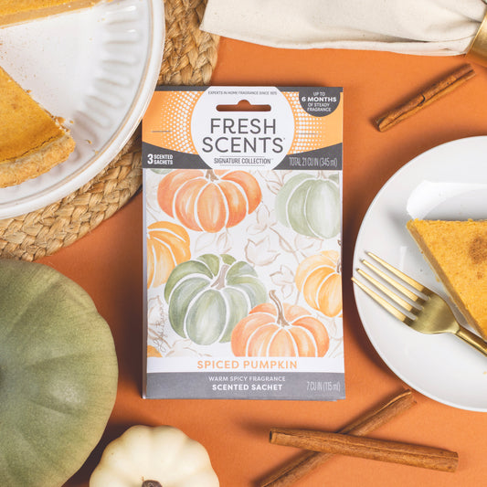 The Fresh Scents Spiced Pumpkin - Sachet 3pk fills an orange surface with flameless fragrance, surrounded by pumpkin pie slices, cinnamon sticks, gold cutlery, and decorative pumpkins.
