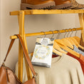 Load image into Gallery viewer, A Fresh Scents Lets Stay Home - Sachet 3pk hangs on a wooden rack among sweaters and tops, with a brown handbag and boots nearby, bringing long-lasting fragrance to the cozy scene.
