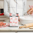 Load image into Gallery viewer, A person in a white apron whisks batter in the kitchen, with decorated Santa cookies, a rolling pin, and a Fresh Scents Merry Santas - Sachet 3pk box for flameless fragrance on the counter.
