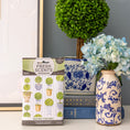 Load image into Gallery viewer, A Fresh Scents Round Topiary - Sachet 3pk rests on a table beside stacked books, a white and blue floral vase with hydrangeas, and a potted round topiary in a blue and white pot—ideal for long-lasting freshness.

