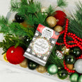 Load image into Gallery viewer, A plastic bin filled with Christmas decorations—green pine branches, red and gold ornaments, red beads, and a Fresh Scents "Wonderful - Sachet 3pk" air freshener labeled “It’s the most wonderful time of the year.”.
