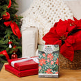 Load image into Gallery viewer, A holiday scene featuring a poinsettia, two red-wrapped gifts, the Fresh Scents Peace on Earth - Sachet 3pk for flameless fragrance, and a decorated Christmas tree in the background beside a chunky knit blanket draped over a chair.
