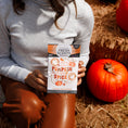 Load image into Gallery viewer, A person in a light gray sweater and brown pants sits on hay with orange pumpkins, holding a Fresh Scents You're the Pumpkin - Sachet 3pk.
