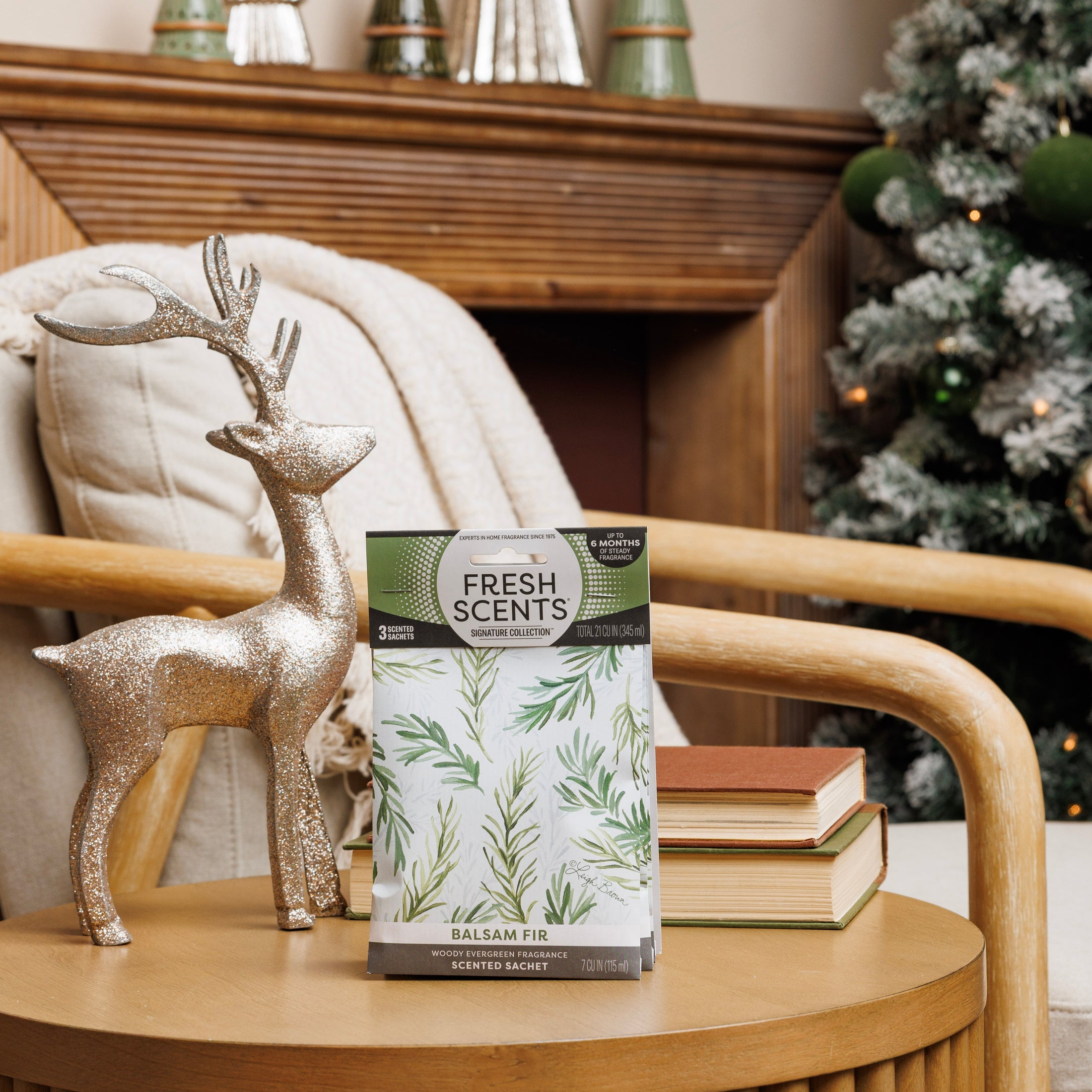 A Fresh Scents Balsam Fir - Sachet 3pk adds flameless fragrance to a wooden chair beside a glittery reindeer, with books, an armchair, and a decorated Christmas tree in the background.