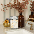 Load image into Gallery viewer, A box of Fresh Scents Fall & Family - Sachet 3pk, a flameless air freshener with long-lasting fragrance, sits on a marble bathroom counter beside a brown glass vase, decorative pumpkins in a gold bowl, and a brass faucet.
