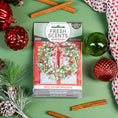 Load image into Gallery viewer, The Fresh Scents Red Door Wreath - Sachet 3pk offers a flameless fragrance and features festive packaging with a holiday wreath, red and green ornaments, cinnamon sticks, pine branch, and a knit cloth on a green background.
