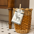 Load image into Gallery viewer, A woven basket rests on a white tiled floor next to a wooden cabinet. A Fresh Scents Woodland Sachet 3pk is clipped to the basket with a clothespin, offering effective, long-lasting flameless fragrance.
