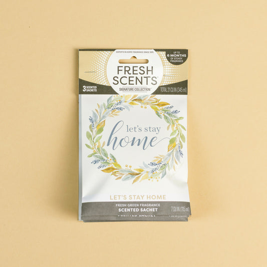 The Fresh Scents Lets Stay Home - Sachet 3pk features a floral wreath design with "let's stay home" on the front—an ideal flameless air freshener that offers long-lasting fragrance, shown here on a plain beige background.
