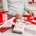 Load image into Gallery viewer, A person in a gray sweater wraps red-and-white gifts with bows and adds a Fresh Scents Merry Santas - Sachet 3pk, a long-lasting air freshener, to one of the presents.
