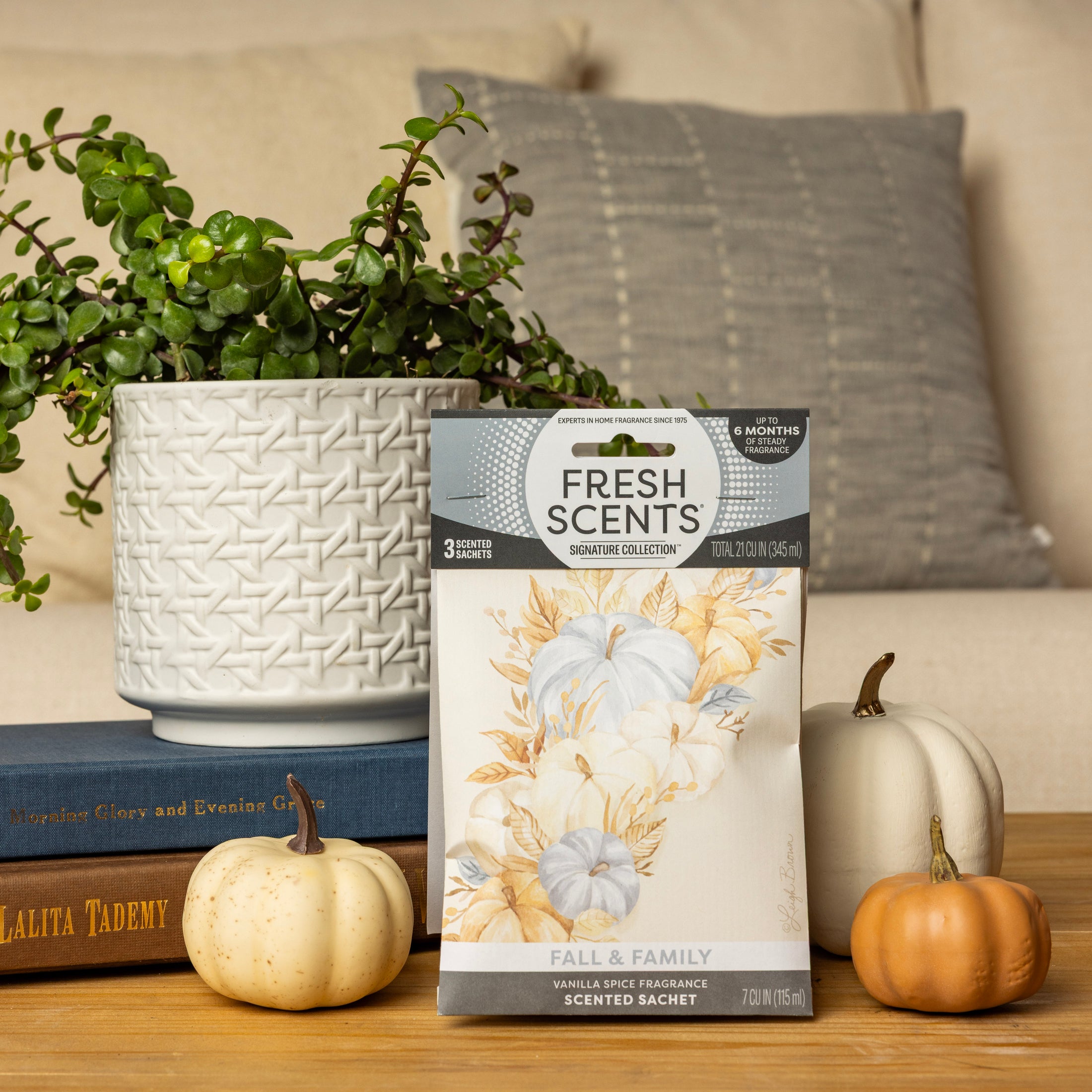 A Fresh Scents Fall & Family - Sachet 3pk rests on a wooden table with pumpkins, books, and a plant nearby, filling the cozy room with long-lasting fragrance—no flame needed.