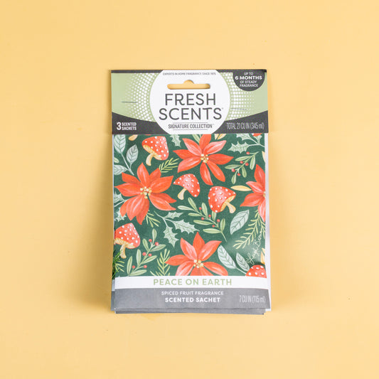 A 3-pack of sachets from Fresh Scents, labeled “Peace on Earth,” features a holiday floral and mushroom design on a yellow background. These sachets offer a spiced fruit fragrance, providing a long-lasting, flameless way to freshen your space.