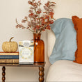 Load image into Gallery viewer, A bedside table displays a small pumpkin, two books, an amber vase with autumn leaves, and a Fresh Scents Lets Stay Home - Sachet 3pk next to a bed adorned with blue and orange pillows.
