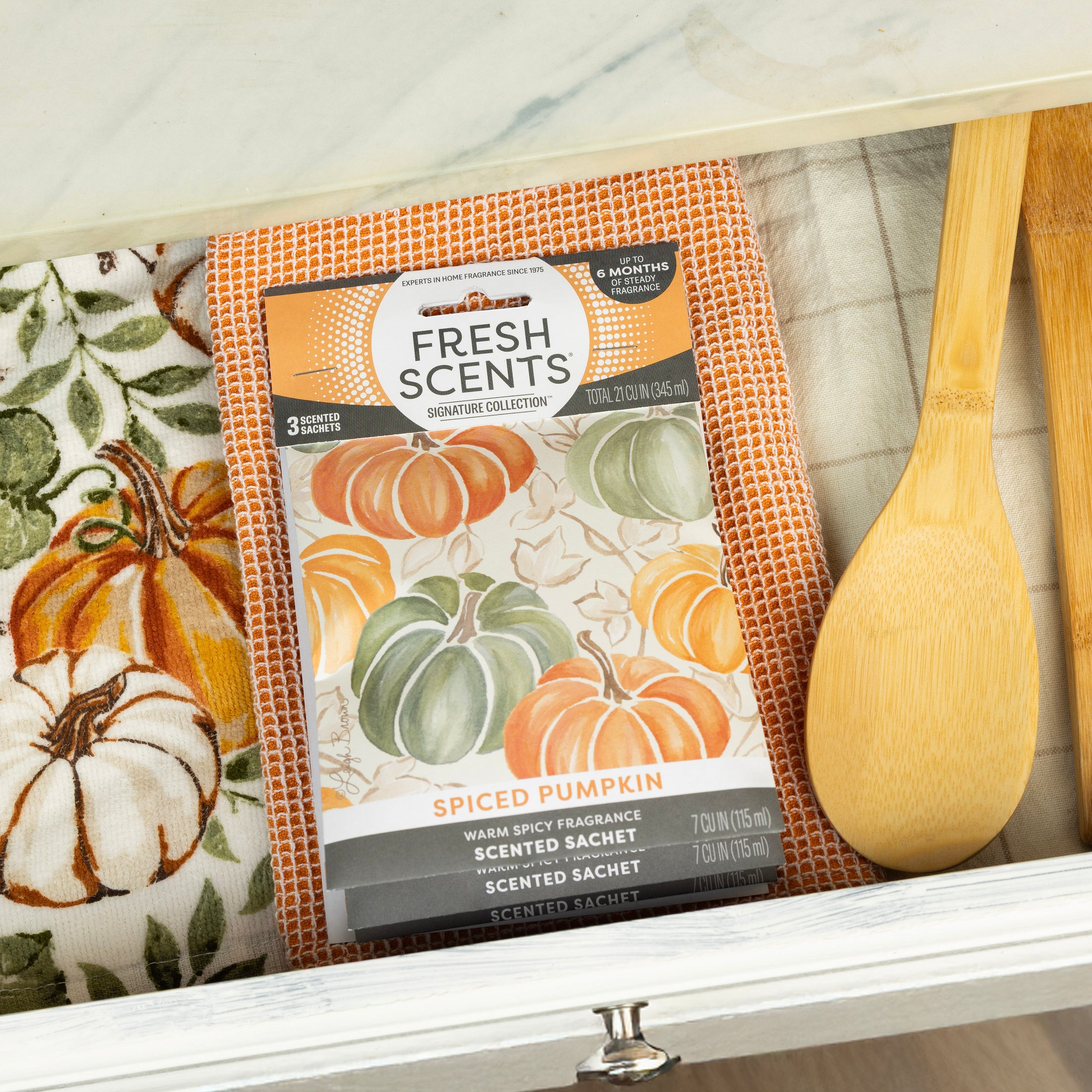 The Fresh Scents Spiced Pumpkin - Sachet 3pk adds long-lasting, flameless fragrance to your space and pairs perfectly with a pumpkin-patterned cloth, orange waffle towel, and wooden utensils for a cozy touch.