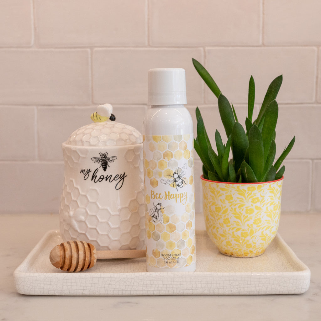 Bee Happy Fragrance in Room Spray Sitting on Countertop with Honey Jar and Fake Plant