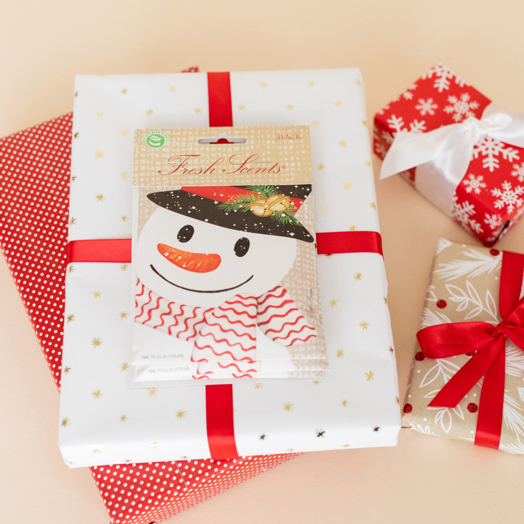 Crafty Snowman Fresh Scents scented sachets on stack of wrapped Christmas gifts.