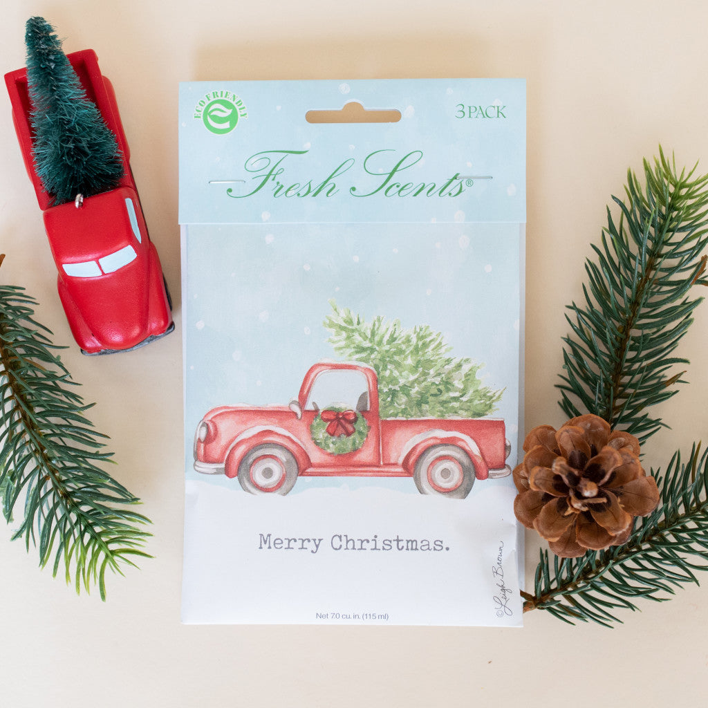 Merry Christmas Fresh Scents scented sachets flat lay with pine needles and red model truck.